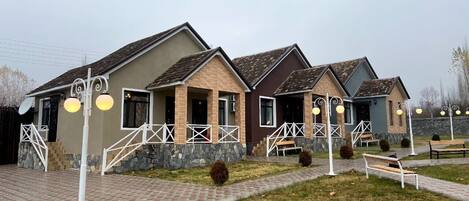 A row of three houses with stone and brick exteriors, white railings, and a paved walkway.