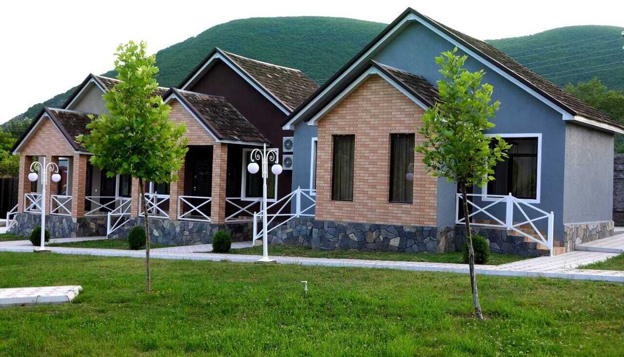 A row of modern, two-story cottages with stone foundations and brick exteriors, set against a backdrop of green hills.