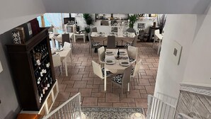 A spacious dining area with multiple tables and chairs, a wine rack, and a staircase leading to an upper level. - descrizione (Fontana Nuova)
