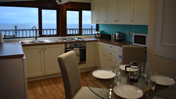A modern kitchen with a view of the sea, equipped with a sink, stove, and microwave. - Cosy bungalow with amazing views  (Filey)