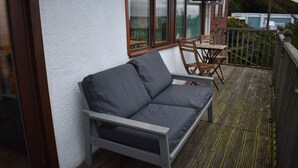 A balcony with a grey sofa, wooden chairs, and a table. - Cosy bungalow with amazing views  (Filey)