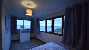 A bedroom with a bed, a dresser, a fan, and large windows offering a view of the sea. - Cosy bungalow with amazing views  (Filey)