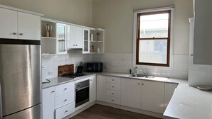 A modern kitchen with white cabinets, a stainless steel refrigerator, a microwave, and a window with blinds. - Saltwater Bungalow - WiFi (Robe)