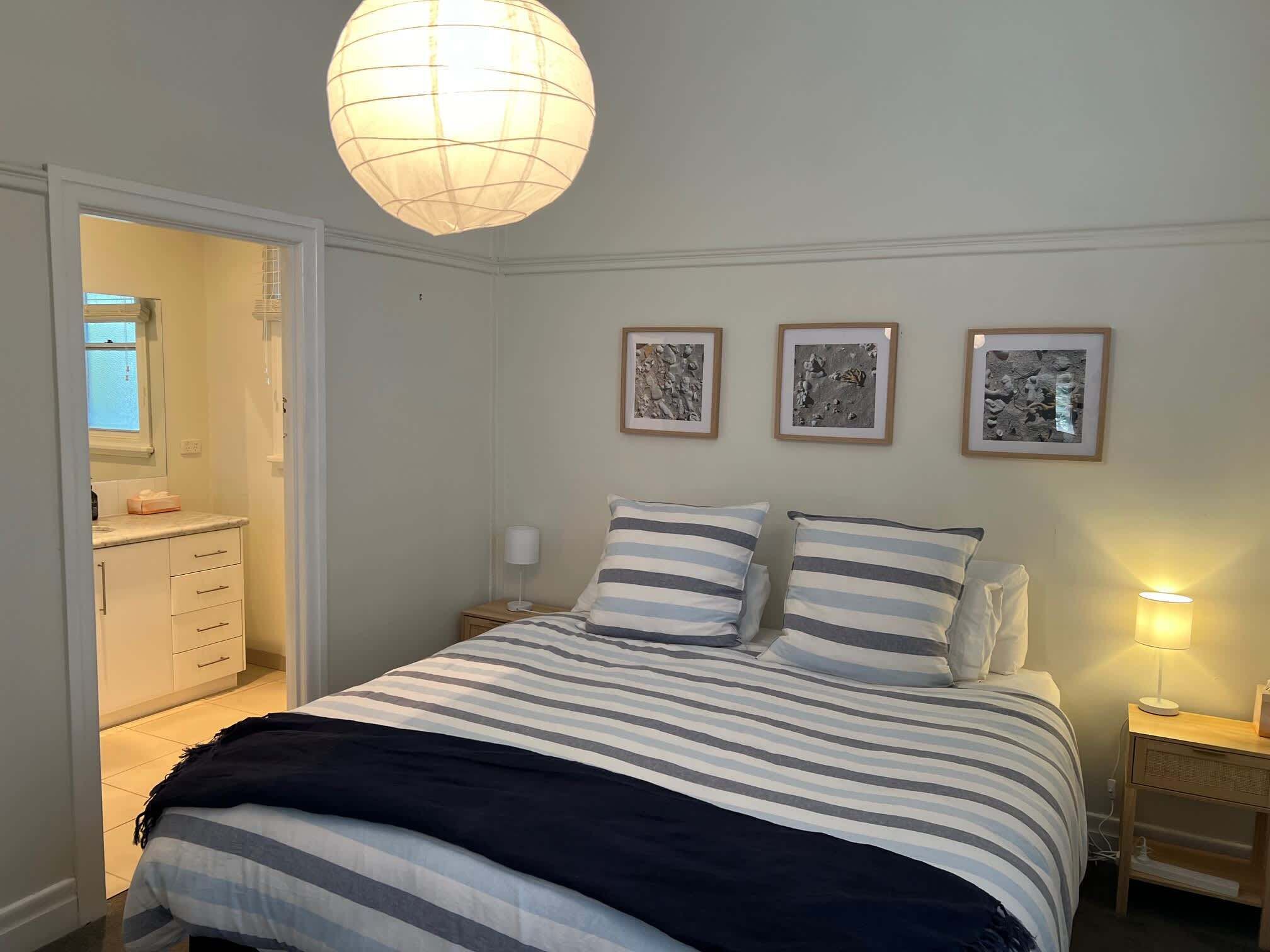 Une chambre à coucher avec un lit, des tables de chevet, un luminaire suspendu et des tableaux encadrés accrochés au mur.