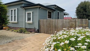 A single-story house with a wooden fence, a paved driveway, and a garden with white flowers. - Saltwater Bungalow - WiFi (Robe)