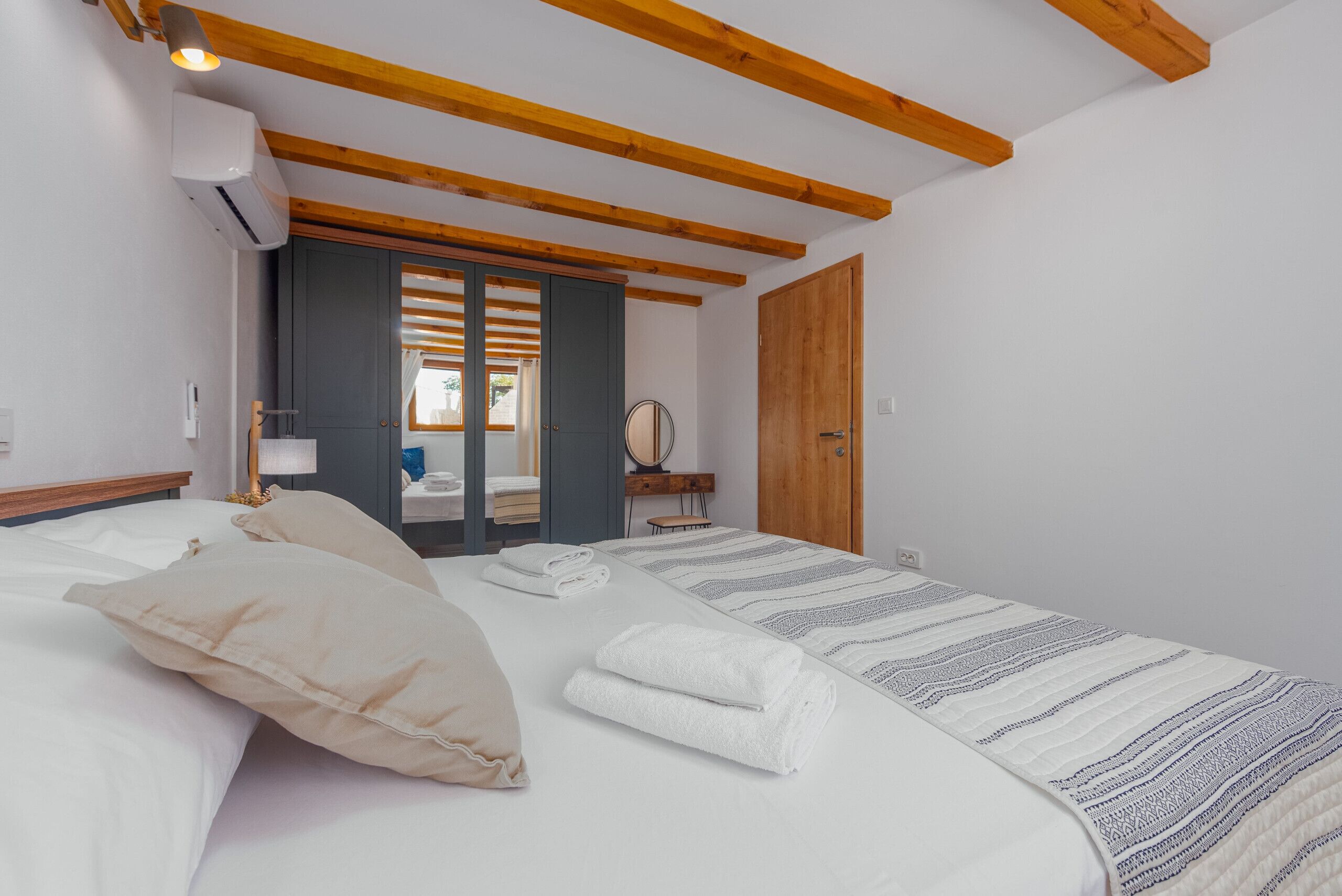 Habitació d'hotel amb un llit, almoines, una taula de nit, un mirall i una porta de fusta.