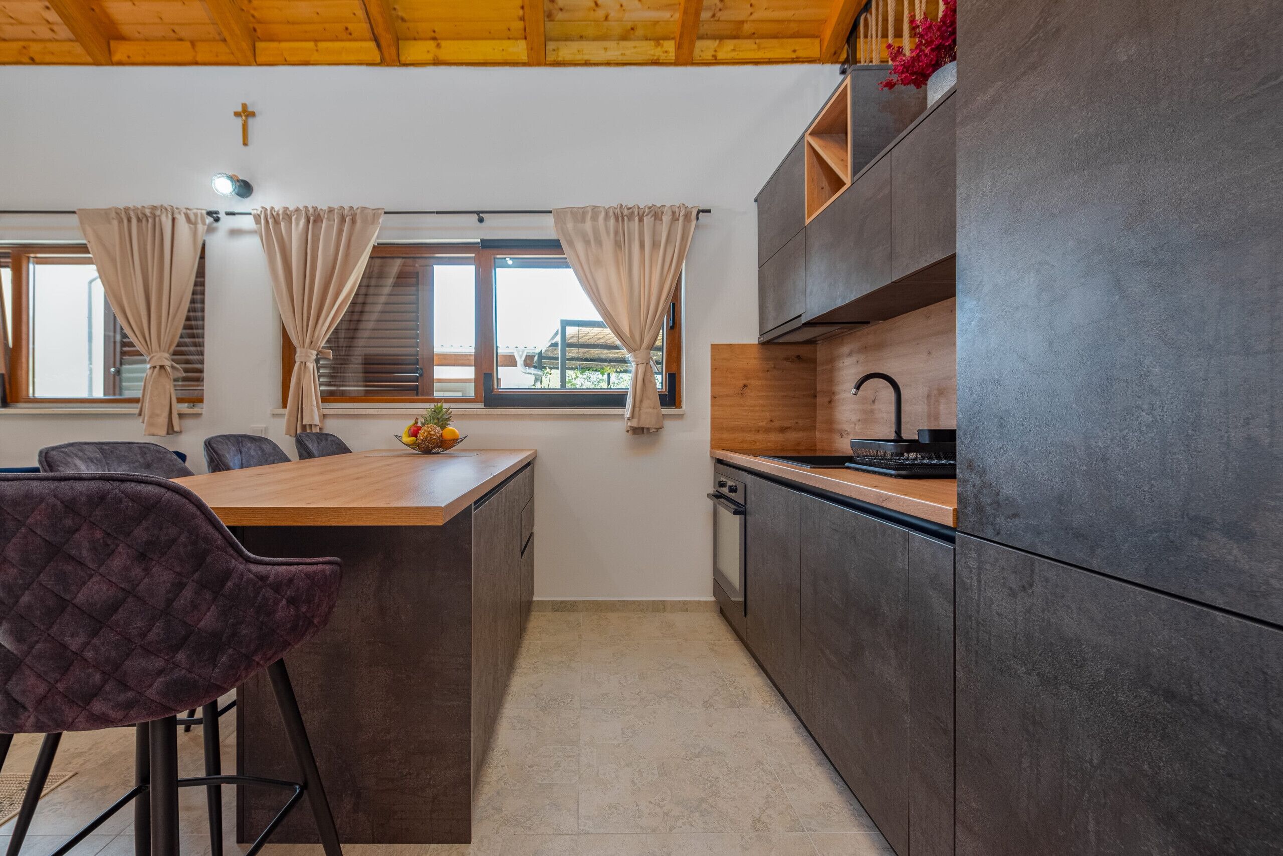 A modern kitchen with a wooden island, dark cabinets, and a view of the outdoors.