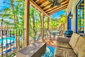 A covered outdoor area with a pool, wicker furniture, and a view of the pool and surrounding greenery. - Overlook Oasis A | 1BR Legacy Villa (La Quinta)