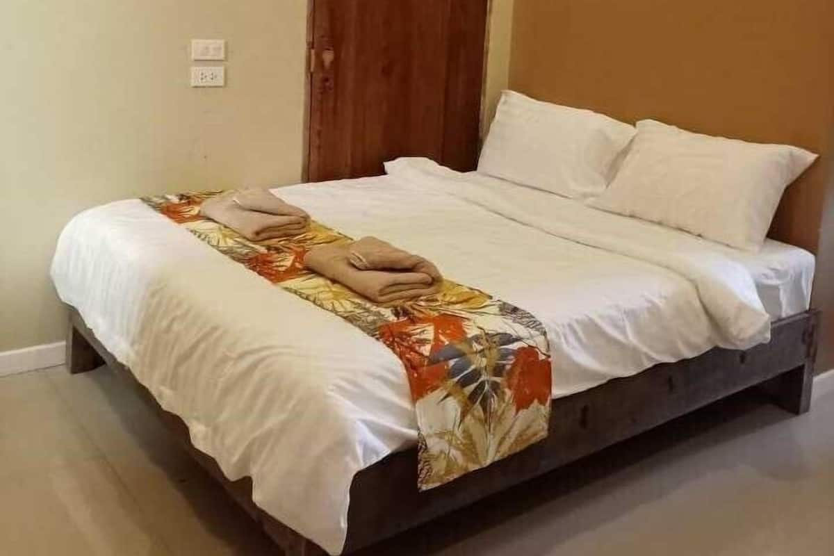 A bed with white linens and a floral-patterned blanket, a wooden door, and a wall-mounted painting.