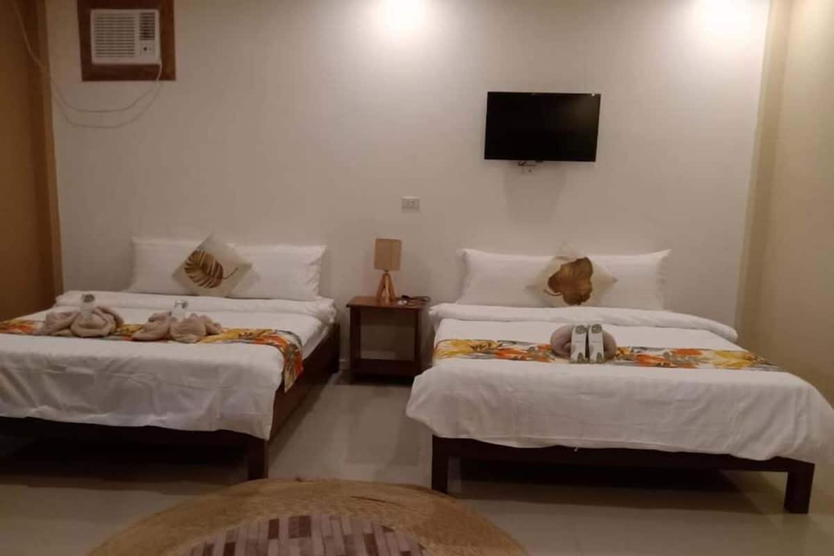A hotel room with two beds, a flat-screen TV, a bedside lamp, and a woven chair.