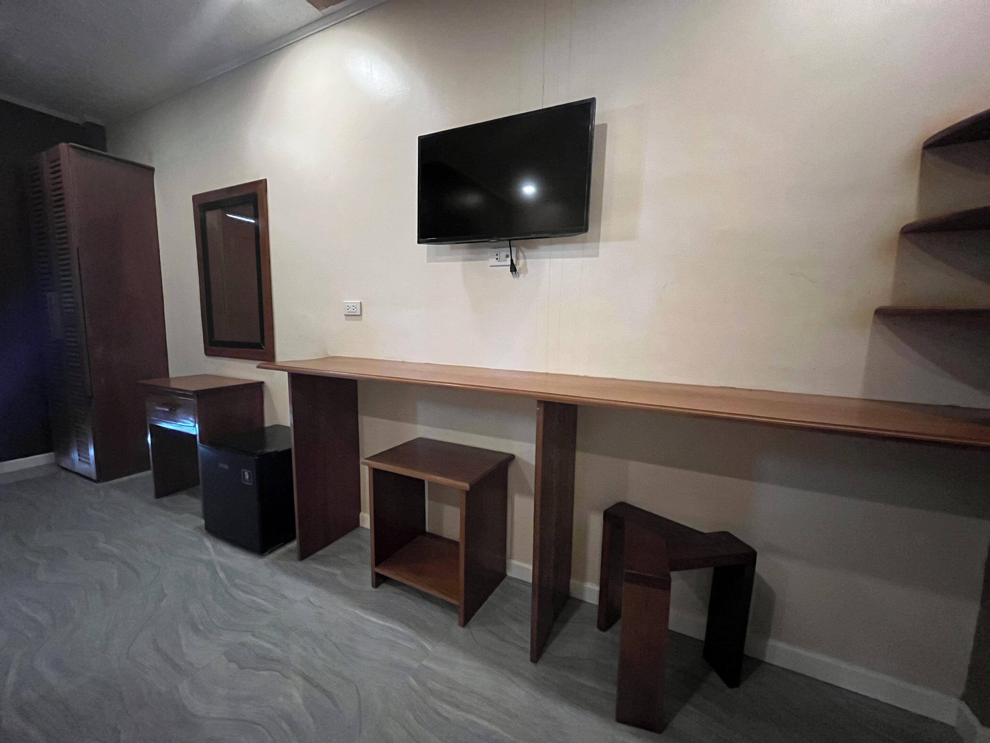 A room with a TV mounted on the wall, a wooden desk, and a shelving unit.