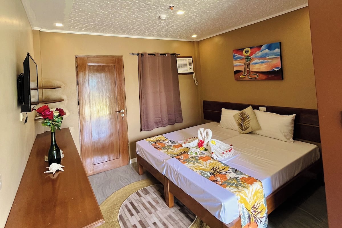 A hotel room with a bed, a desk, a vase with flowers, a painting on the wall, and a ceiling with a textured pattern.