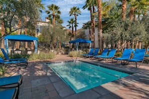 A swimming pool with blue lounge chairs and umbrellas, surrounded by palm trees and greenery. - The Desert Loft | 2BR Legacy Villa (La Quinta)