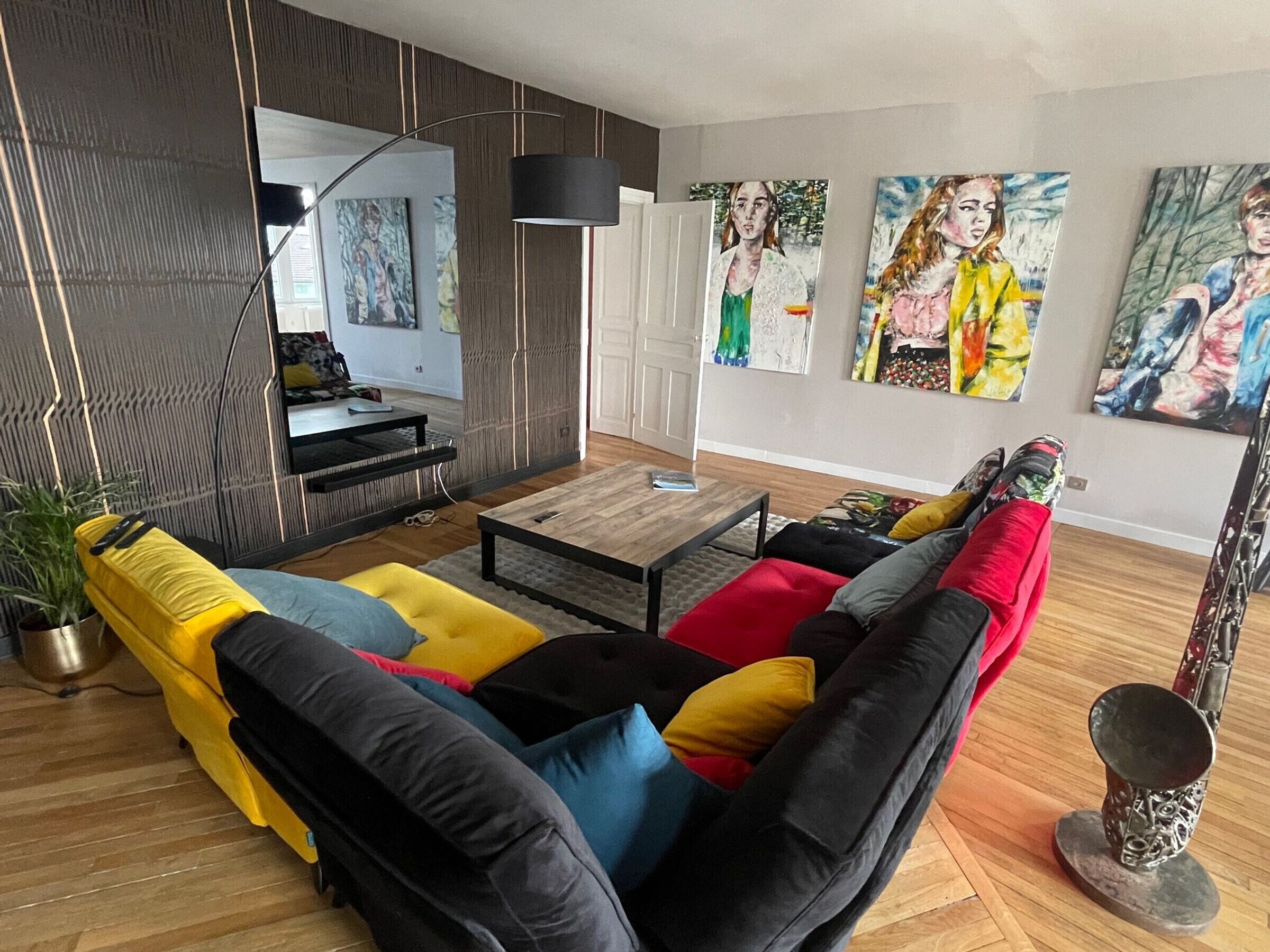 A modern living room with a sectional sofa, a coffee table, and a TV. There are paintings on the wall and a plant on the floor.
