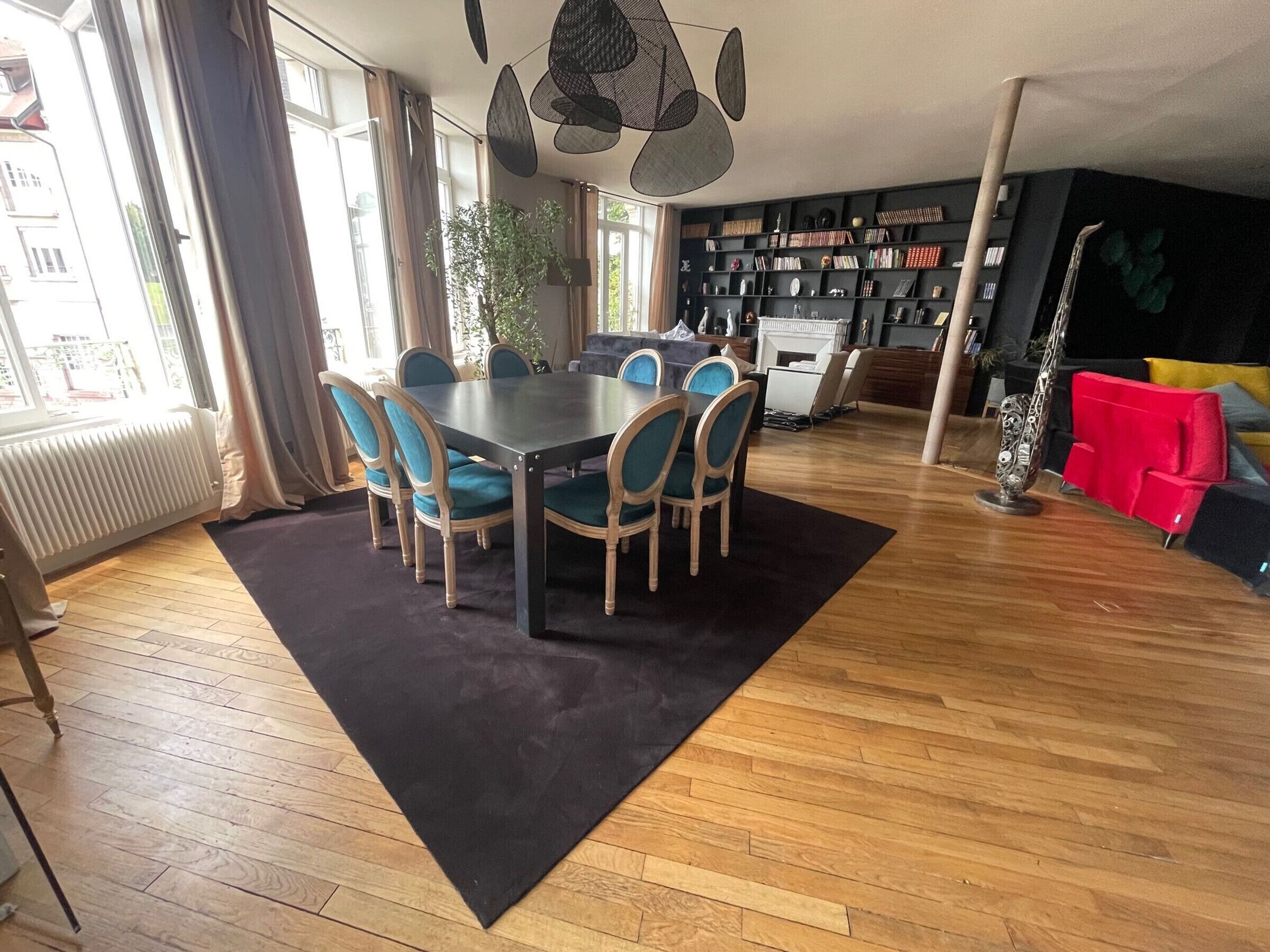 A dining area with a round table and chairs, a bookshelf, a red sofa, and a radiator.