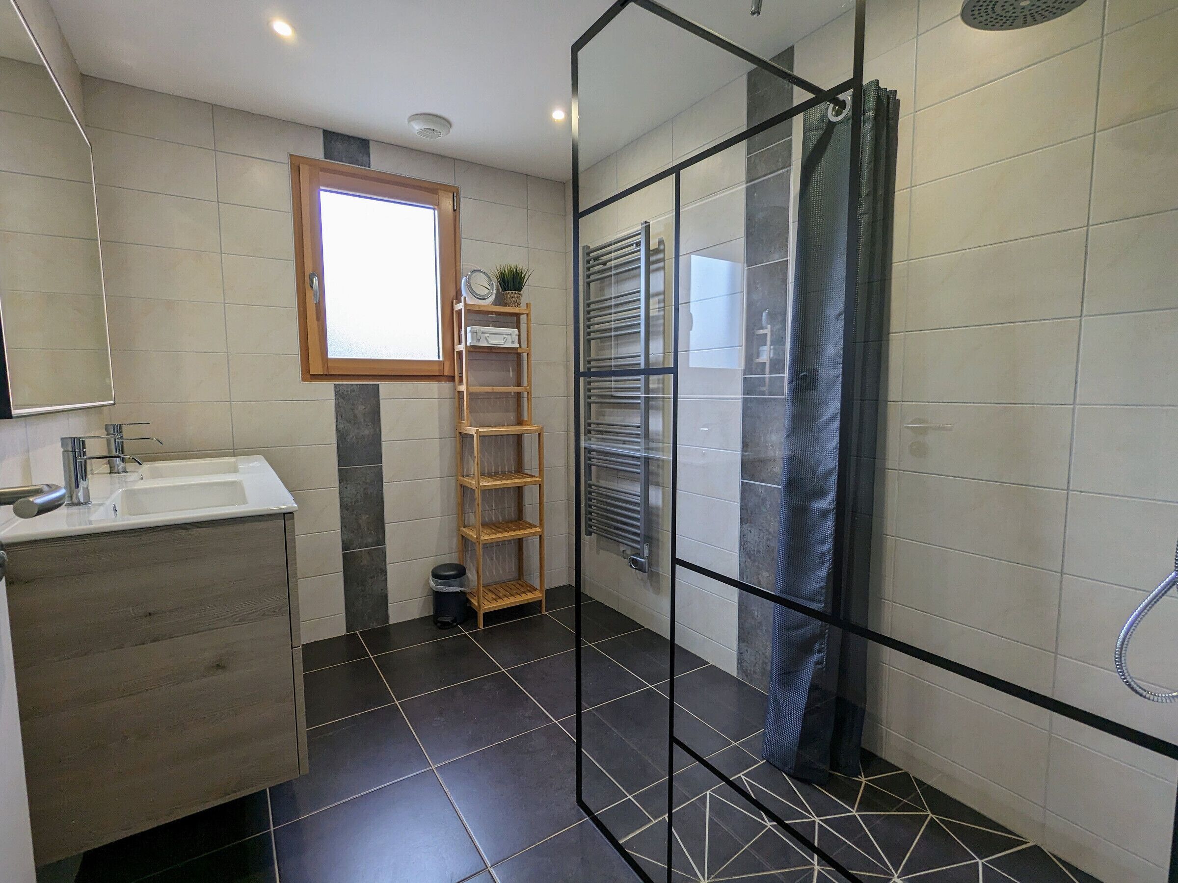 Une salle de bain moderne avec une douche à l’italienne en verre, un meuble-lavabo en bois et une petite fenêtre.