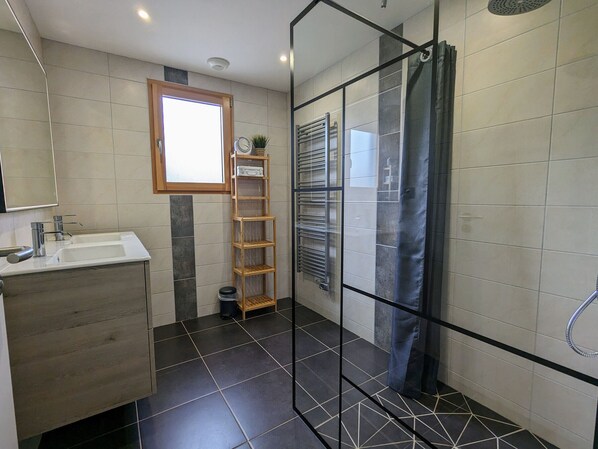 A modern bathroom with a glass shower enclosure, a wooden vanity, and a small window.