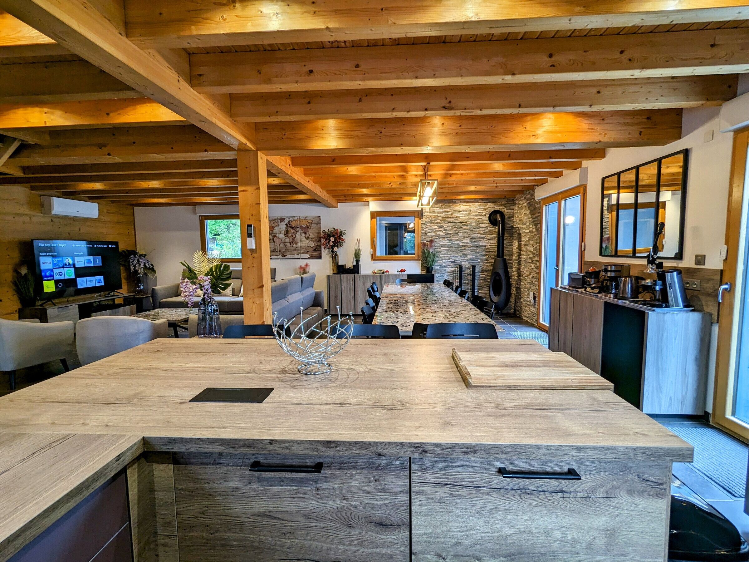 Una cocina moderna con una isla grande, vigas de madera, detalles de piedra y una chimenea empotrada.