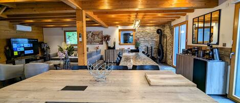 Una cocina moderna con una isla grande, vigas de madera, detalles de piedra y una chimenea empotrada.