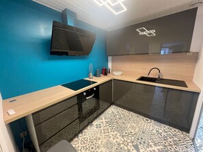 A modern kitchen with a blue wall, black cabinets, a black countertop, and a patterned floor. - Cozy apartment in Épinal, near attractions (Épinal)