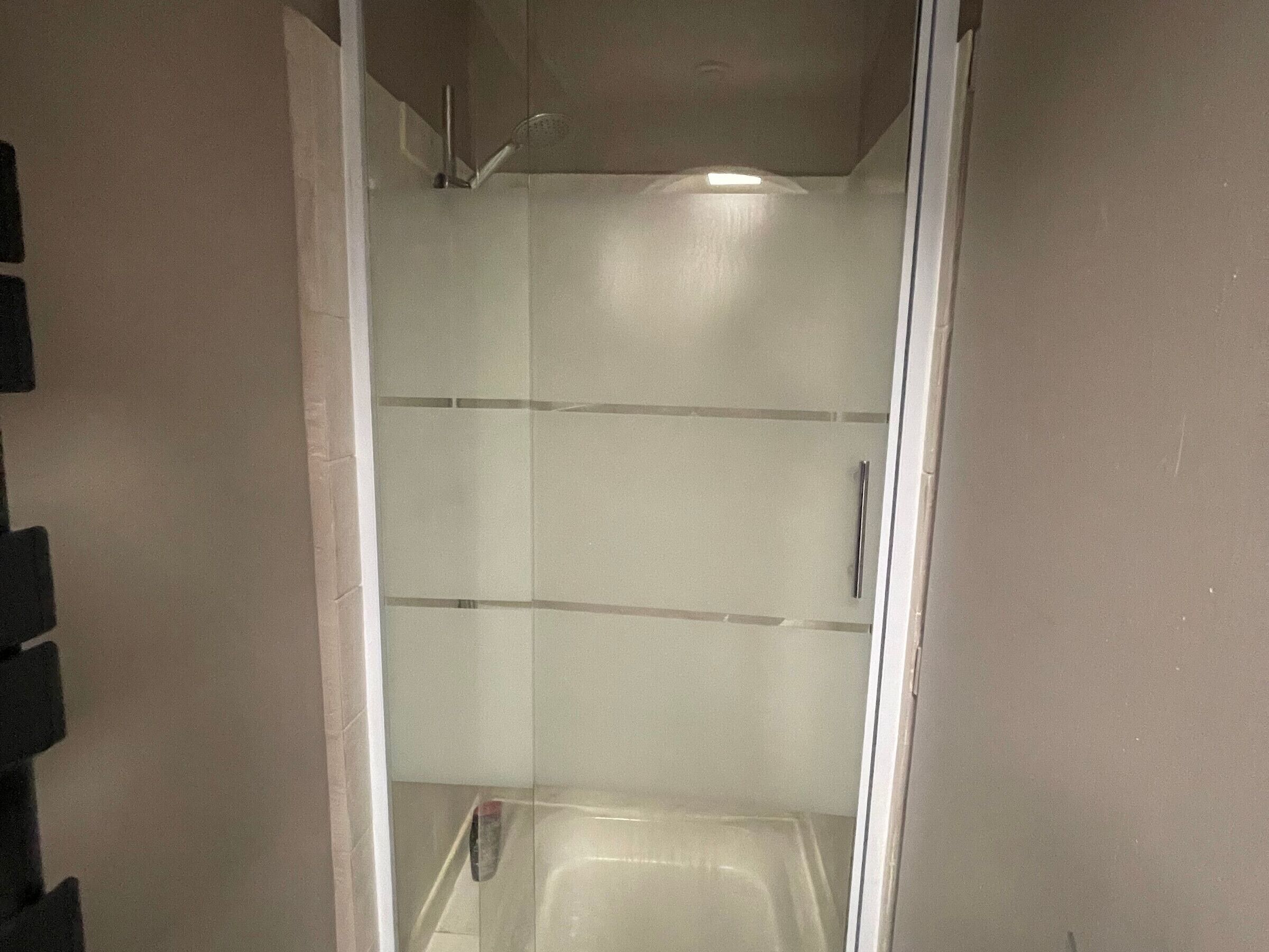 A glass-enclosed shower stall with a handheld showerhead and a vertical handle.