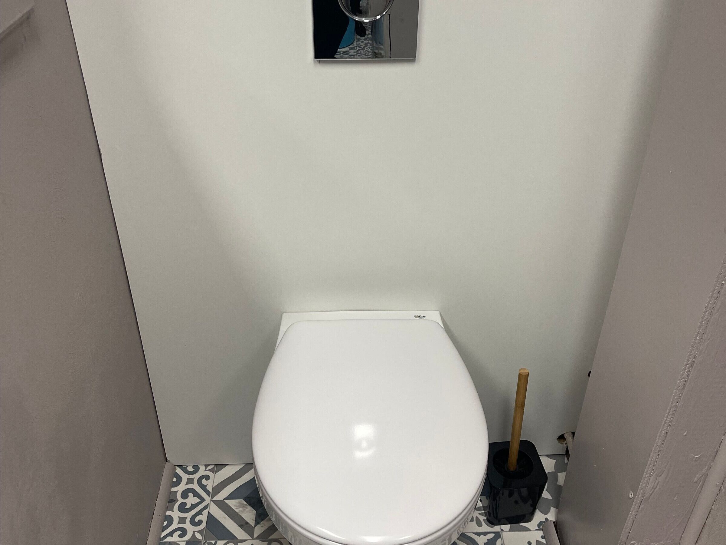 A small, compact bathroom with a white toilet, a toilet brush, and a patterned floor.