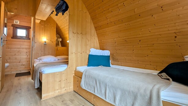 Una habitación tipo cabaña acogedora, con paredes de madera y techo inclinado, que incluye dos camas y un ventanal pequeño.