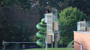 Un parque infantil con un tobogán en espiral, una zona vallada y un edificio de techo plano.