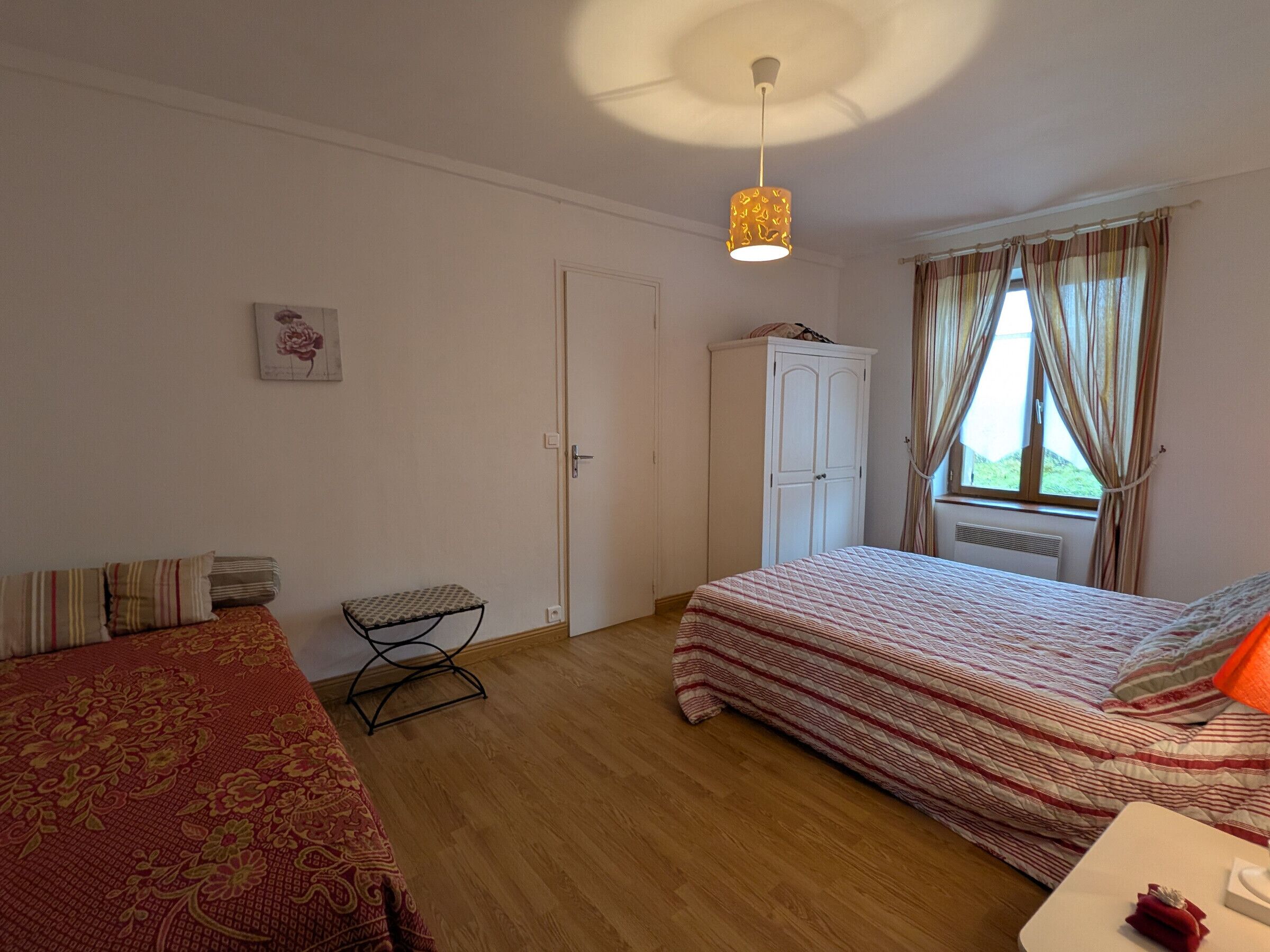 A bedroom with a bed, a chair, a wardrobe, and a window with curtains.