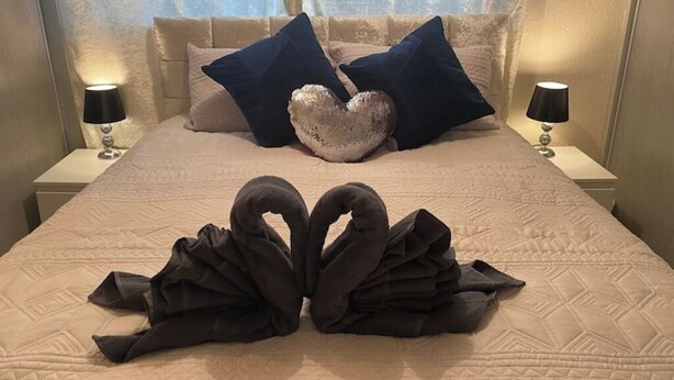 A neatly made bed with a heart-shaped pillow and two swan-shaped towels on the bed.