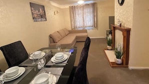 A dining area with a table set for four, a sofa, and a clock on the wall.