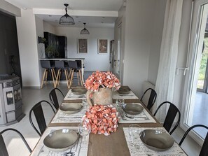 A dining area with a long table set for six, surrounded by chairs. There is a kitchen in the background with a dining table and chairs. - Spacious house with spa, pets allowed, near Épinal (Dounoux)