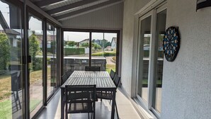 A covered patio with a table and chairs, large sliding glass doors, and a dartboard on the wall. - Spacious house with spa, pets allowed, near Épinal (Dounoux)