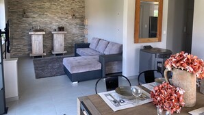 A modern living room with a stone wall, a grey sofa, a wooden coffee table, and a dining area with a table set for two. - Spacious house with spa, pets allowed, near Épinal (Dounoux)