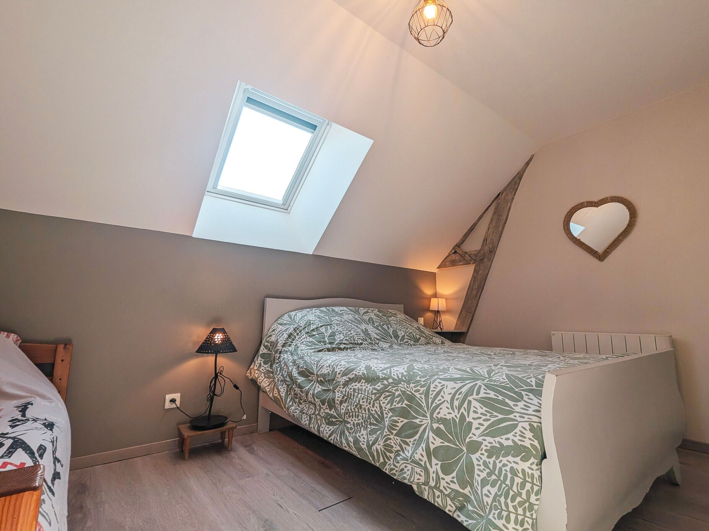 Una camera da letto con un lucernario, un letto con copriletto decorato, una lampada da comodino e uno specchio a forma di cuore sulla parete.