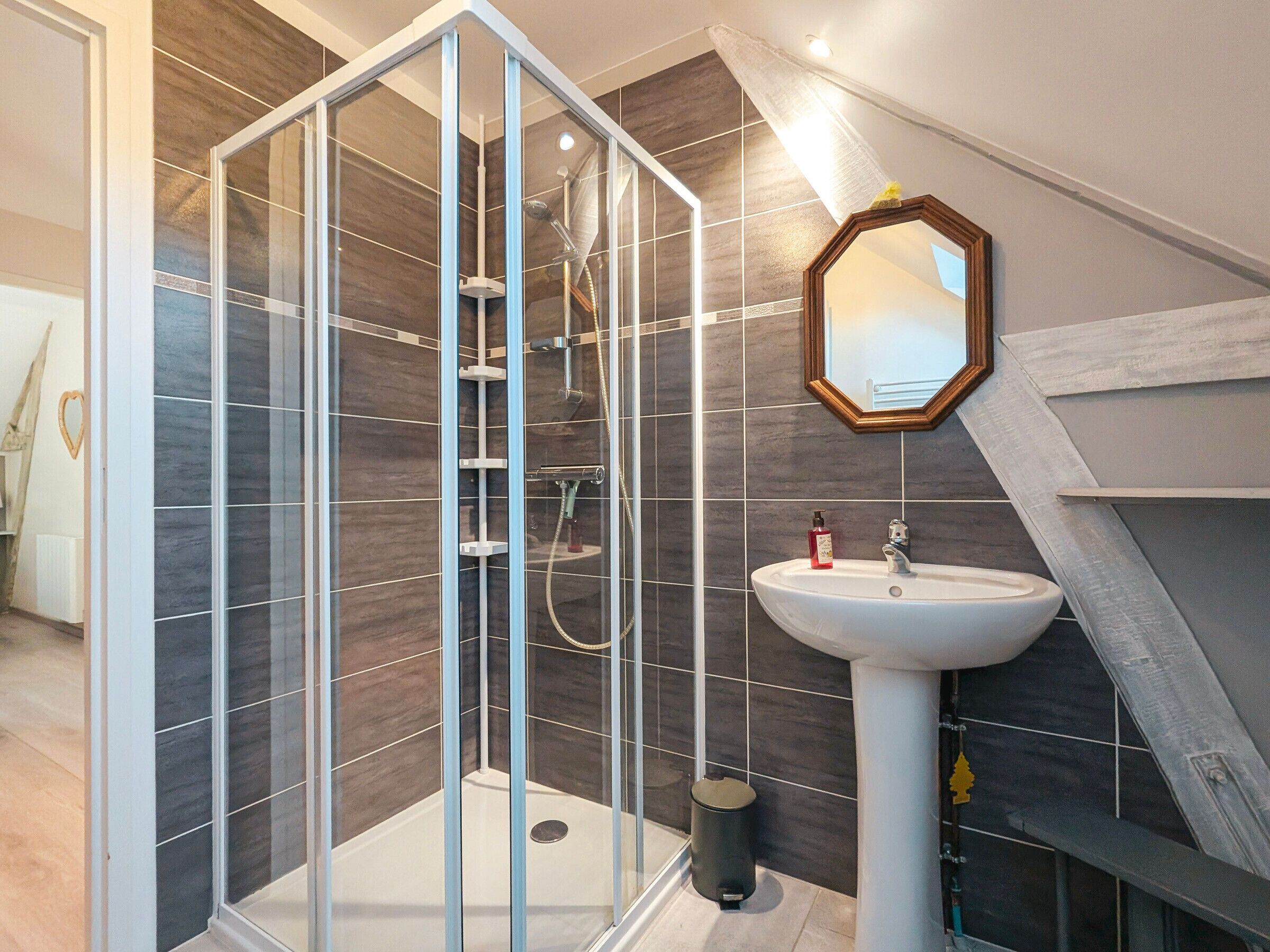 Een moderne badkamer met een douche in een glazen cabine, een witte wasbak en een spiegel met houten lijst.