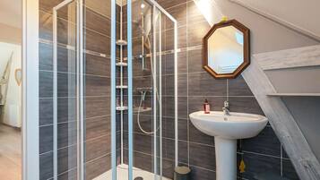 Een moderne badkamer met een douche in een glazen cabine, een witte wasbak en een spiegel met houten lijst.