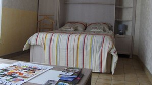 A bedroom with a bed, a nightstand, a wardrobe, and a table with magazines. - Cozy studio in Nancy, near center, wifi included (Nancy)