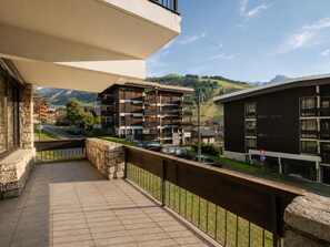 A balcony with a stone wall, a view of a multi-story building, and a road with cars.