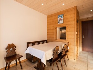 Una habitación de madera con una cama, una mesa y sillas. Hay un cartel en la pared y una puerta a la derecha.