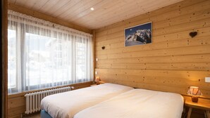 A wooden-paneled room with a large bed, a window with sheer curtains, a picture of a mountain, and a heart-shaped decoration on the wall. - 3* Apartment near slopes and shops, Wi-Fi (La Clusaz)