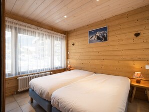 A wooden-paneled room with a large bed, a window with sheer curtains, a picture of a mountain, and a heart-shaped decoration on the wall.