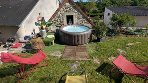 Un patio trasero con un jacuzzi, una construcción de piedra y dos sillas plegables rojas.