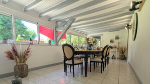 Un comedor con piso de baldosas, una mesa de madera y sillas. Hay un jarrón con flores sobre la mesa, y un farol en una mesita.