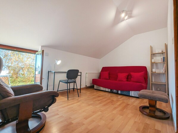 Een kamer met een rode bank, een bureau met stoel, een houten vloer en een boekenkast.