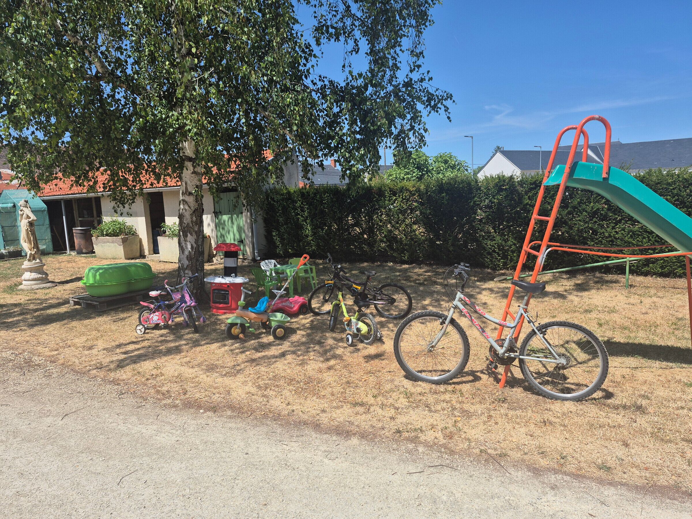 A backyard with a bicycle, a green play structure, and a statue.