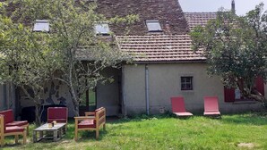 A rustic building with a tiled roof, a small window, and a door. There are two red chairs and a wooden table with candles.