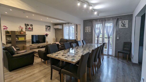 Un salon moderne comprenant un coin repas, un canapé, un téléviseur et une grande fenêtre avec des rideaux.