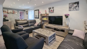Un salon moderne doté d’un grand téléviseur à écran plat, de canapés en cuir, d’une table basse et d’un coin repas à l’arrière-plan.