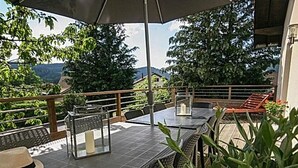 Une terrasse extérieure avec des tables et des chaises, entourée de verdure et offrant une vue sur un paysage montagneux.